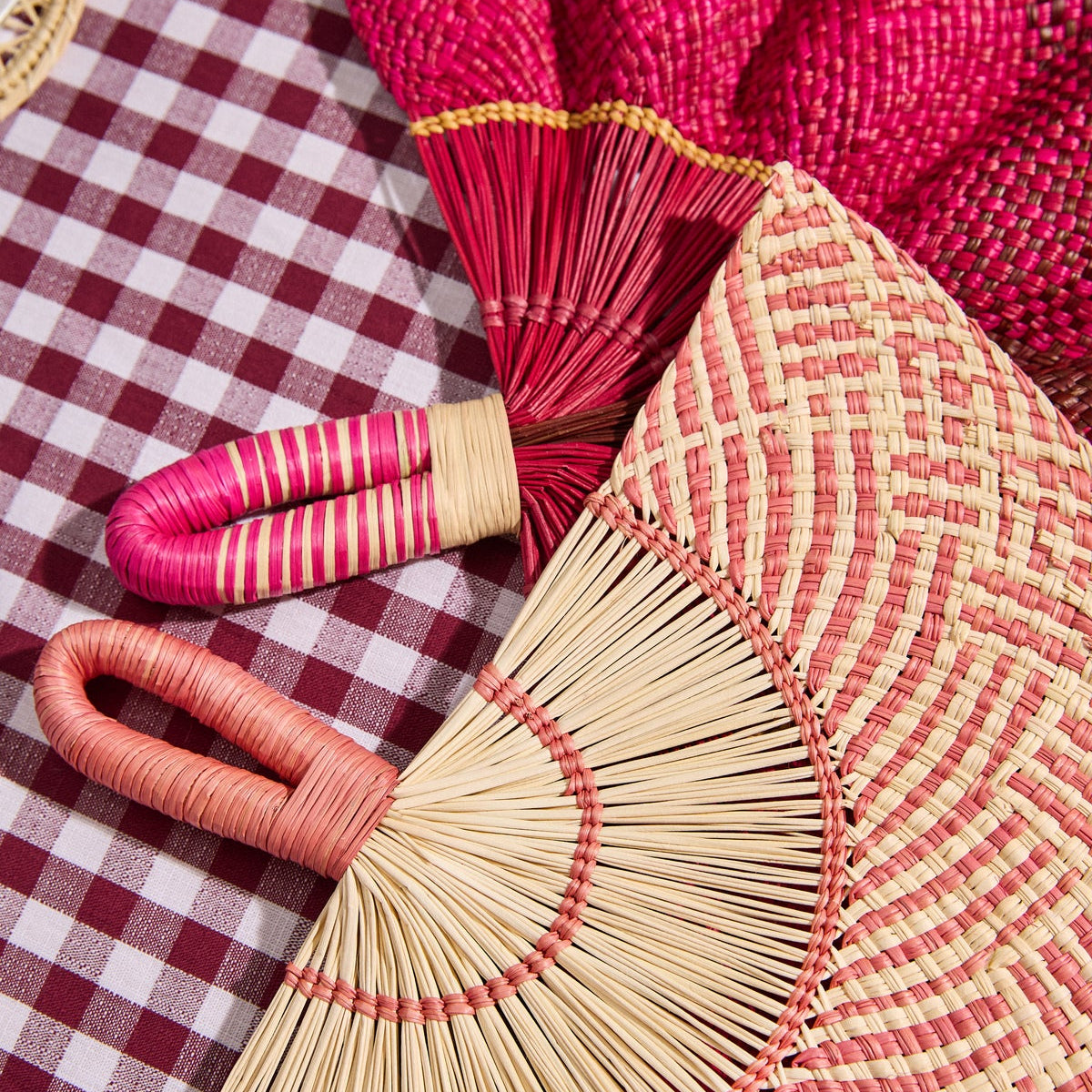 Handwoven fans and a woven placemat on a burgundy gingham tablecloth
