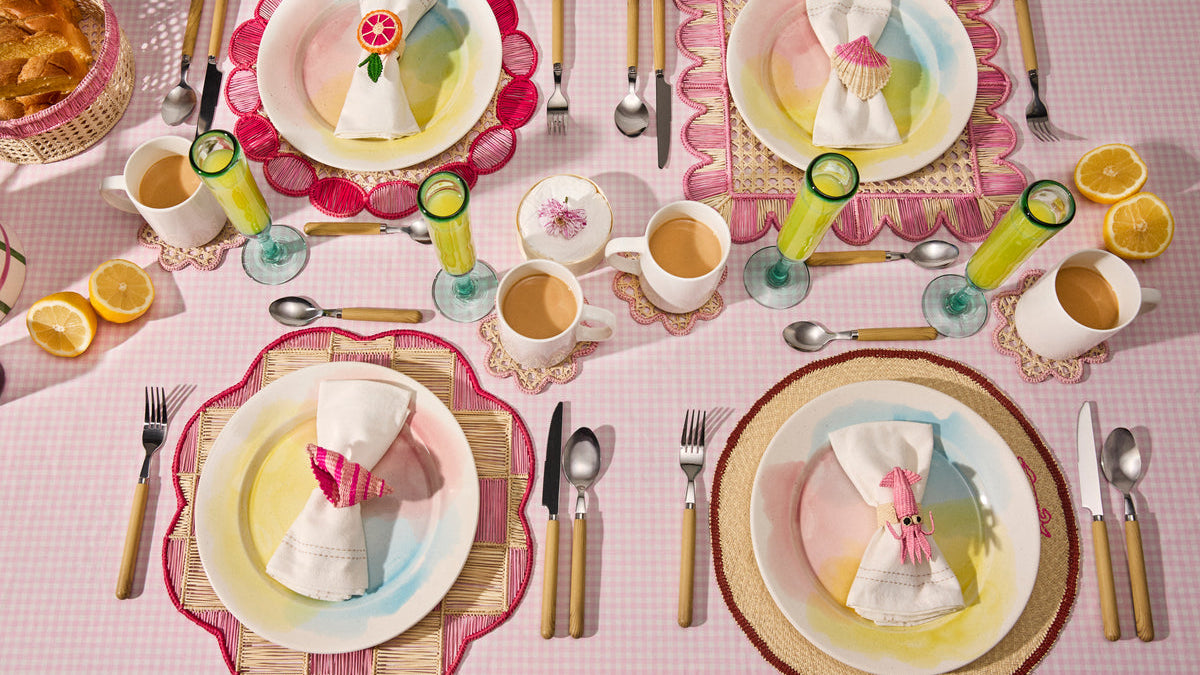 Pastel pink table with four place settings, handwoven placemats and floral napkin rings