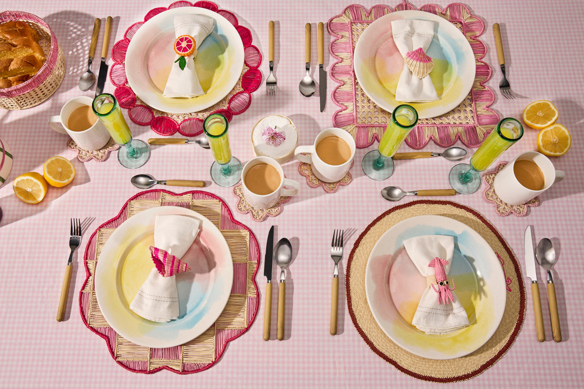 Pastel pink table with four place settings, handwoven placemats and floral napkin rings