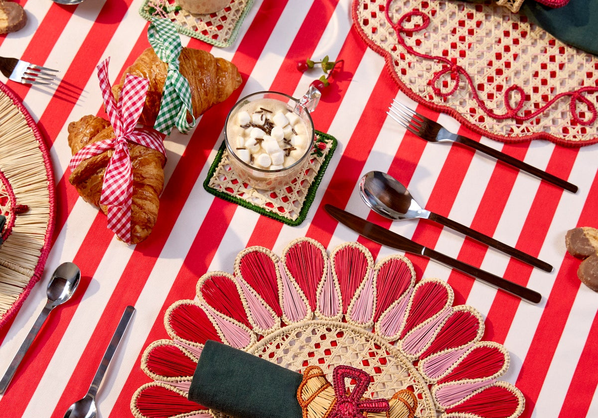 Holiday table with handwoven placemats and napkin rings on a red and white striped tablecloth