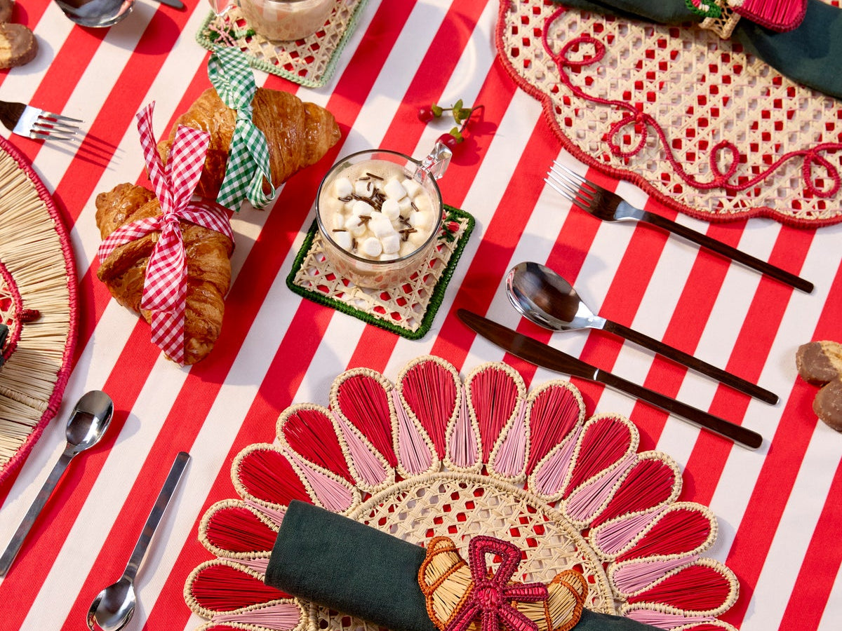 Holiday table with handwoven placemats and napkin rings on a red and white striped tablecloth